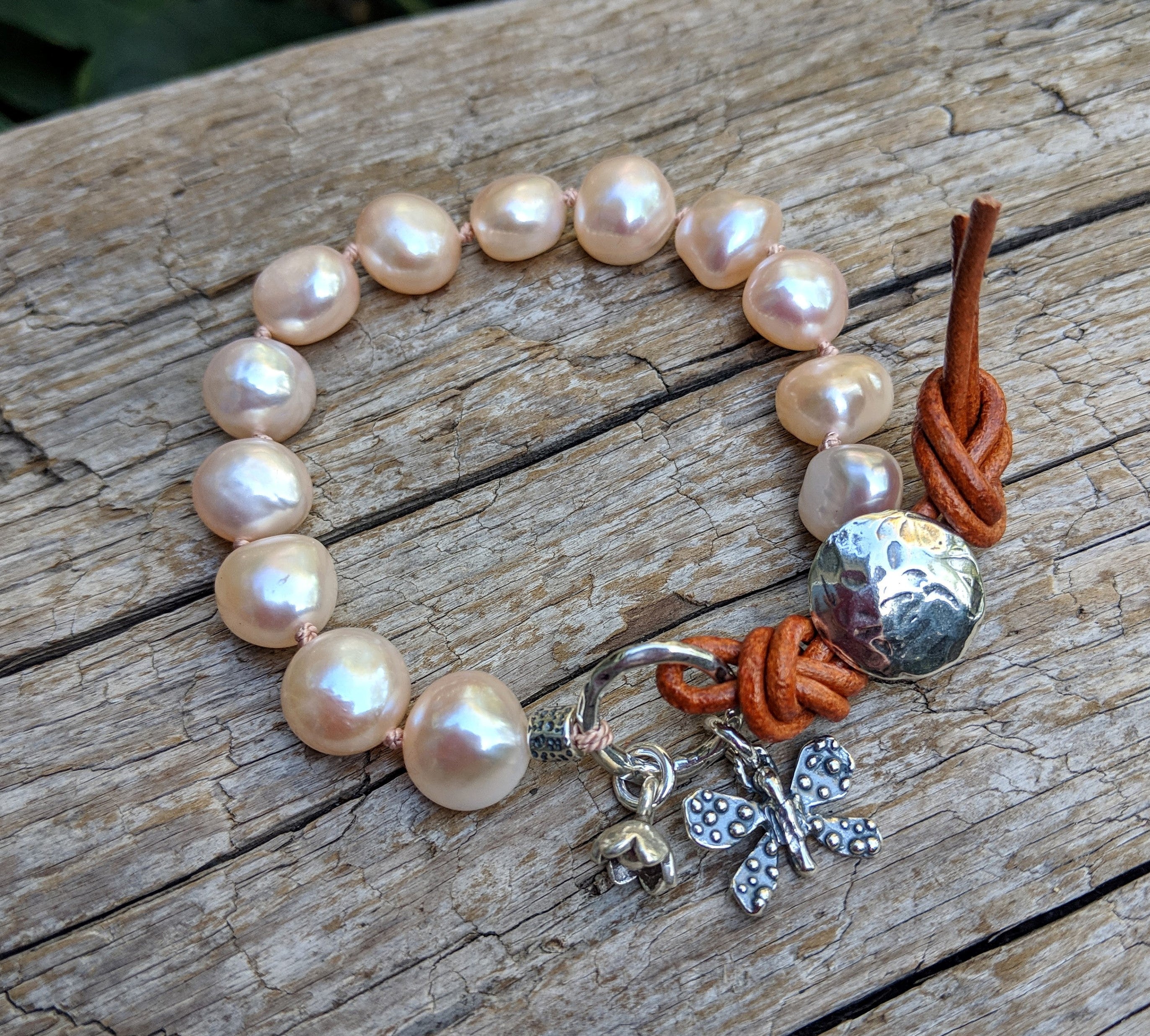 This beautiful one-of-a-kind chic handmade artisan bracelet combines beautiful soft pink-peach baroque pearls with sterling silver flower and butterfly charms, accented by leather elements for an organic look. The beautiful natural rose pink shades radiate chic femininity, staying true to nature. 