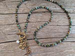 This beautiful handmade artisan piece showcases the deep green and brown colors of African turquoise, complimented by gold bronze elements. The artisan crowned heart and dream gold bronze charms create a fun touch and a dream theme to the piece.  This piece can be worn as a necklace or a wrap bracelet. 