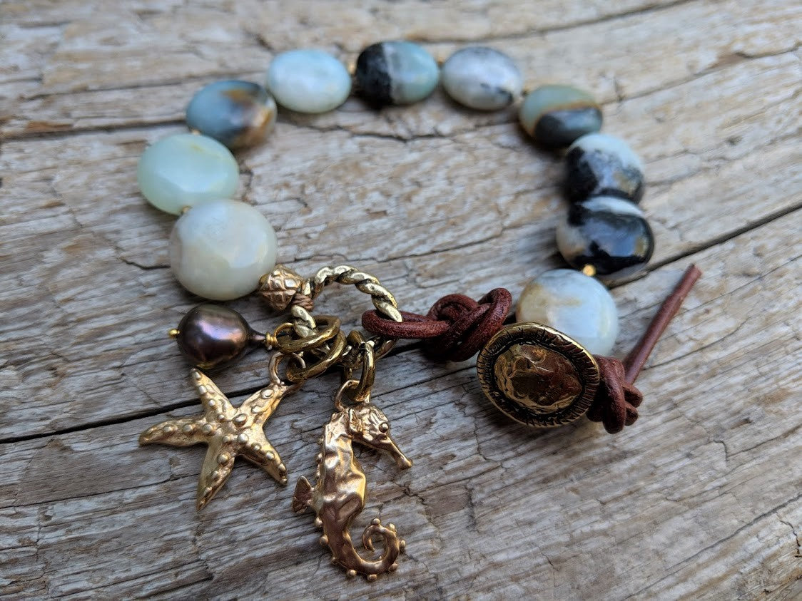 This beautiful handmade artisan bracelet showcases the beauty of natural amazonite gemstone. The calm blues, mints, grays, and natural beiges of amazonite feel refreshing complimented by gold bronze ocean-themed starfish and seahorse charms. The black pearl is suspended together with the charms to match some of the colors found within the stone. Feel like you are taking a relaxing walk on the beach with this beautiful one-of-a-kind ocean-themed bracelet.