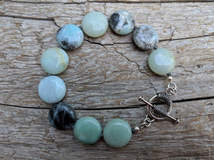 This beautiful handmade artisan toggle bracelet showcases the beauty of natural amazonite gemstone. The calm blues, mints, grays, and natural beiges of amazonite feel refreshing complimented by sterling silver elements. The bracelet was designed with simplicity in mind, to keep the focus on the natural textures of the beautiful stone.