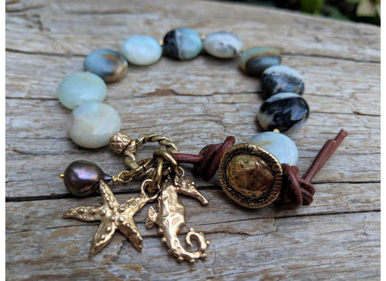 This beautiful handmade artisan bracelet showcases the beauty of natural amazonite gemstone. The calm blues, mints, grays, and natural beiges of amazonite feel refreshing complimented by gold bronze ocean-themed starfish and seahorse charms. The black pearl is suspended together with the charms to match some of the colors found within the stone. Feel like you are taking a relaxing walk on the beach with this beautiful one-of-a-kind ocean-themed bracelet.