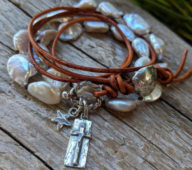 This handmade artisan one-of-a-kind bracelet combines the gorgeous white-gray baroque pearls with sterling silver and leather elements. The bracelet is held together by a silk thread and a light brown leather cord. The silver button, cross and star charms add a beautiful shine to the combination and create a religious theme.