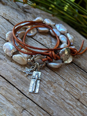 This handmade artisan one-of-a-kind bracelet combines the gorgeous white-gray baroque pearls with sterling silver and leather elements. The bracelet is held together by a silk thread and a light brown leather cord. The silver button, cross and star charms add a beautiful shine to the combination and create a religious theme.