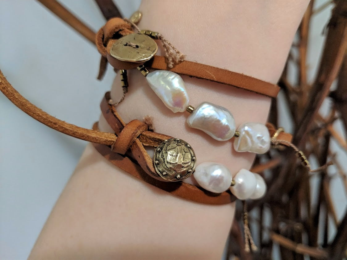 Handmade boho natural baroque pearl leather wrap bracelet with gold bronze button and heart charm. The artisan bracelet is adjustable as leather knots can be moved for a perfect fit. The gold bronze heart charm can freely move along the leather cord. A modern take on boho chic style jewelry showcasing natural pearls and leather.