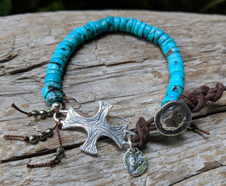 A vibrant modern handmade artisan one-of-a-kind bracelet showcasing the beauty of natural textures. The intoxicating blue turquoise is complemented beautifully by the leather color and texture. Sterling silver cross adds some shine to the combination and creates a religious theme. Tiny pyrite beads add more texture and natural sparkle.